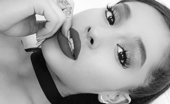 Ariana Grande z tatuażami na rękach i szyi, czarno-białe zdjęcie.
