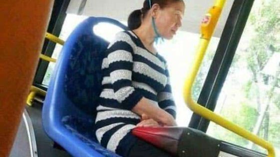 Kobieta z metalowym naczyniem na głowie siedzi na autobusowym siedzeniu.