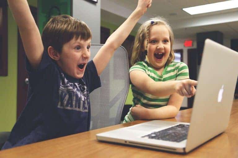Dzieci z radością oglądają ekran laptopa podczas gry online.