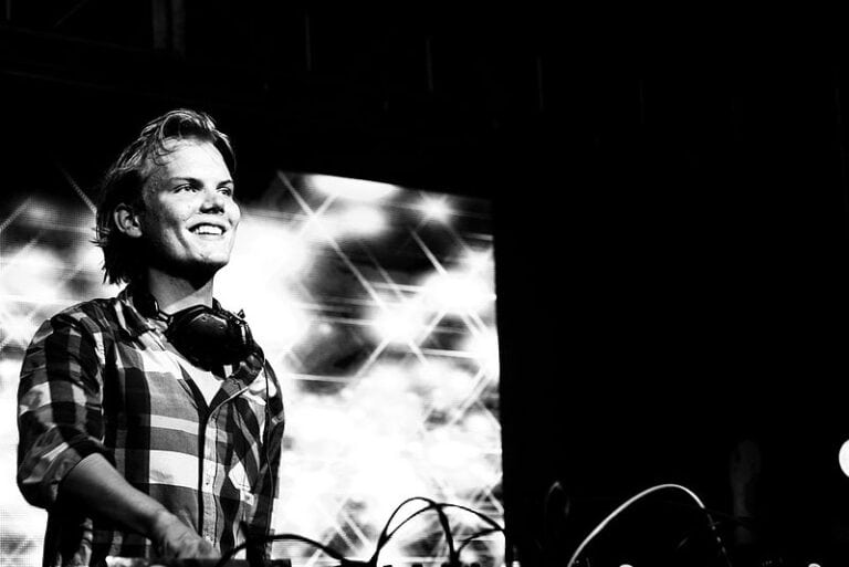 DJ Avicii na scenie, uśmiechnięty, w czarno-białym ujęciu.