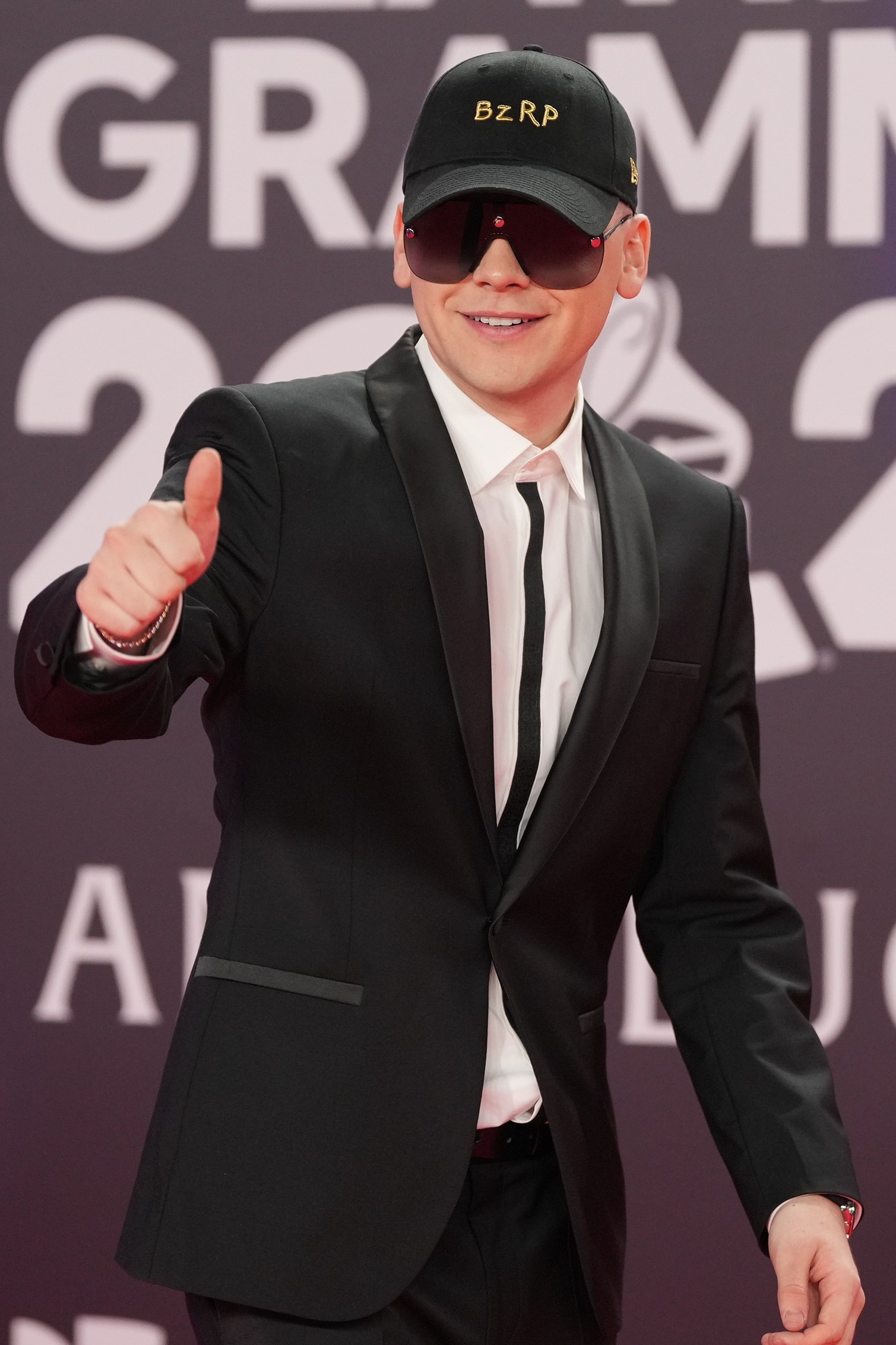 Bizarrap na Latin Grammy 2023 w czarnej czapce Bizarrap na czerwonym dywanie Latin Grammy 2023 w czarnym garniturze, okularach i czapce BZRP pokazuje kciuk do góry