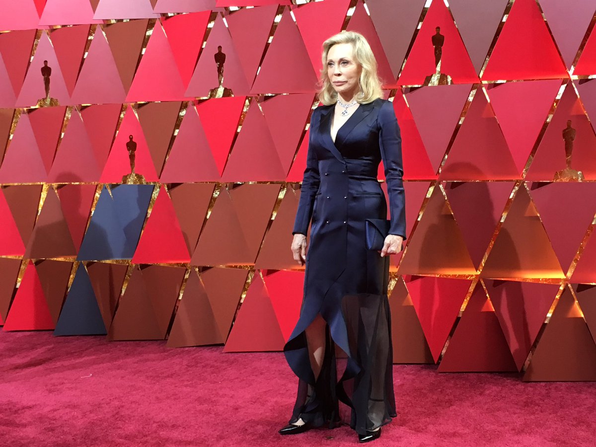 Faye Dunaway na czerwonym dywanie podczas Oscarów 2017, w granatowej sukni na tle złotych statuetek