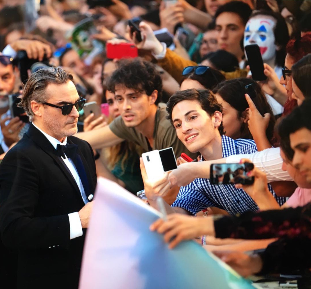 Joaquin Phoenix w czarnym garniturze i okularach rozmawia z fanami na czerwonym dywanie 76. Festiwalu Filmowego w Wenecji