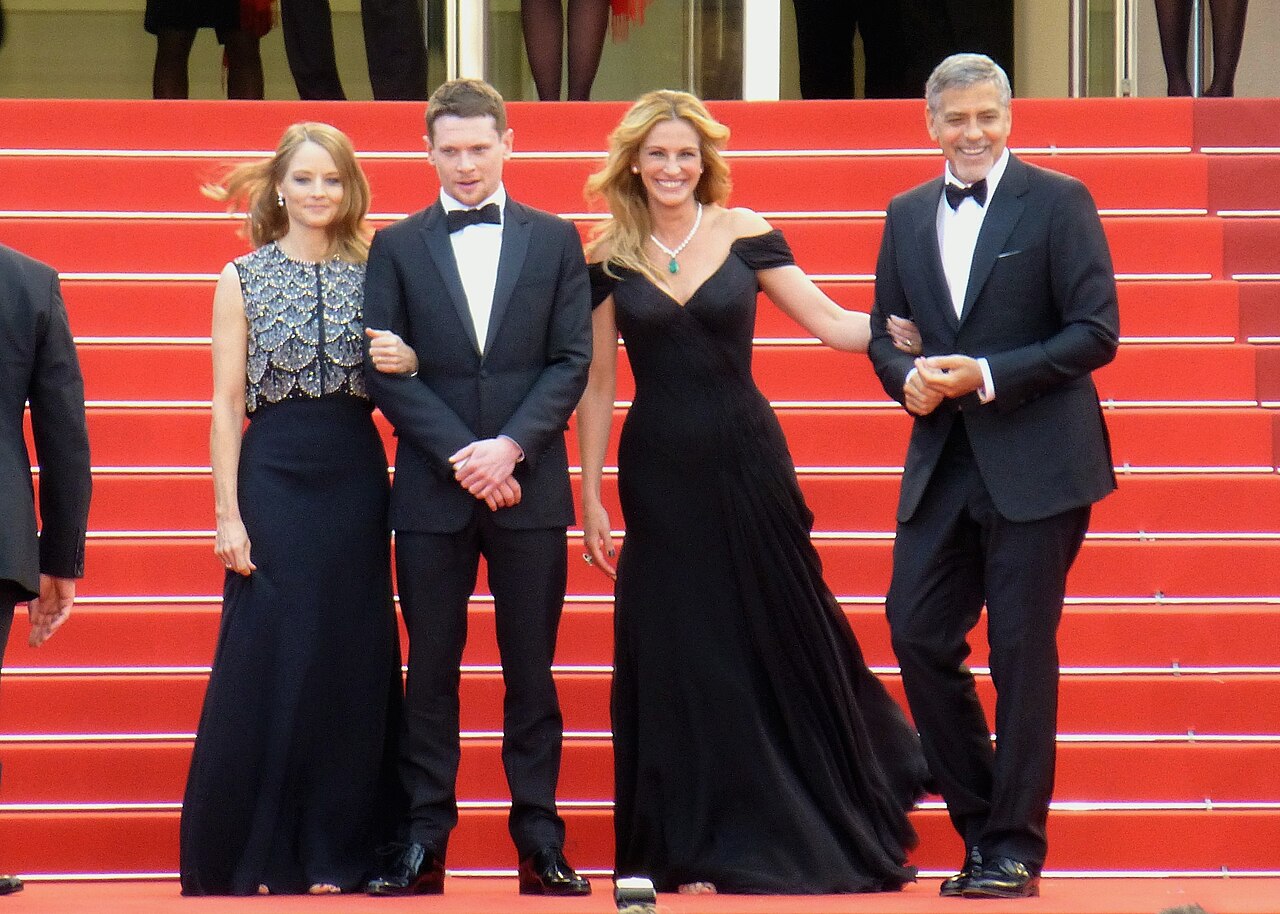 Julia Roberts stoi w czarnej sukni obok George'a Clooneya i Jacka O'Connella podczas premiery Money Monster w Cannes 2016, spod sukni widoczne są bose stopy
