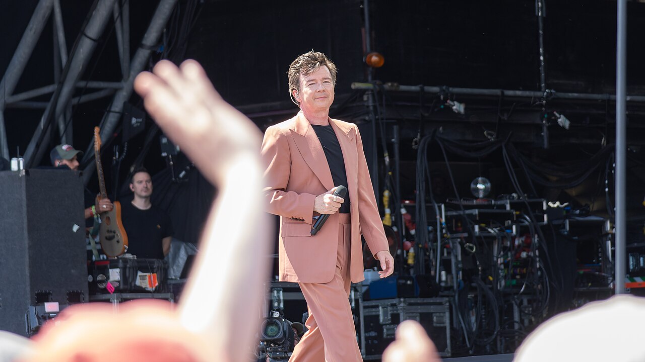 Rick Astley na głównej scenie festiwalu Glastonbury 2023 Rick Astley podczas występu na Pyramid Stage w Glastonbury w różowym garniturze, 24 czerwca 2023 roku
