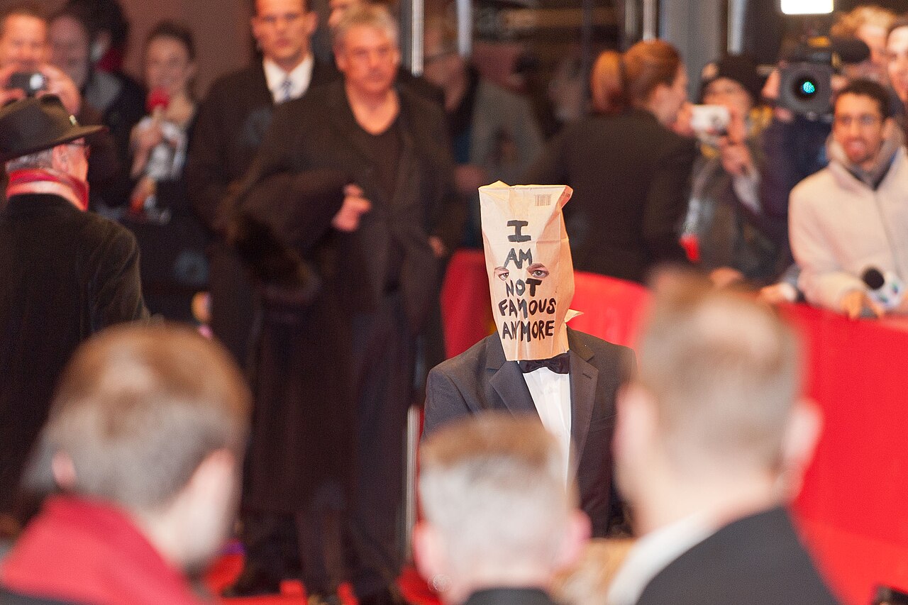 Shia LaBeouf w czarnym smokingu i z papierową torbą na głowie z napisem I AM NOT FAMOUS ANYMORE podczas Berlinale 2014