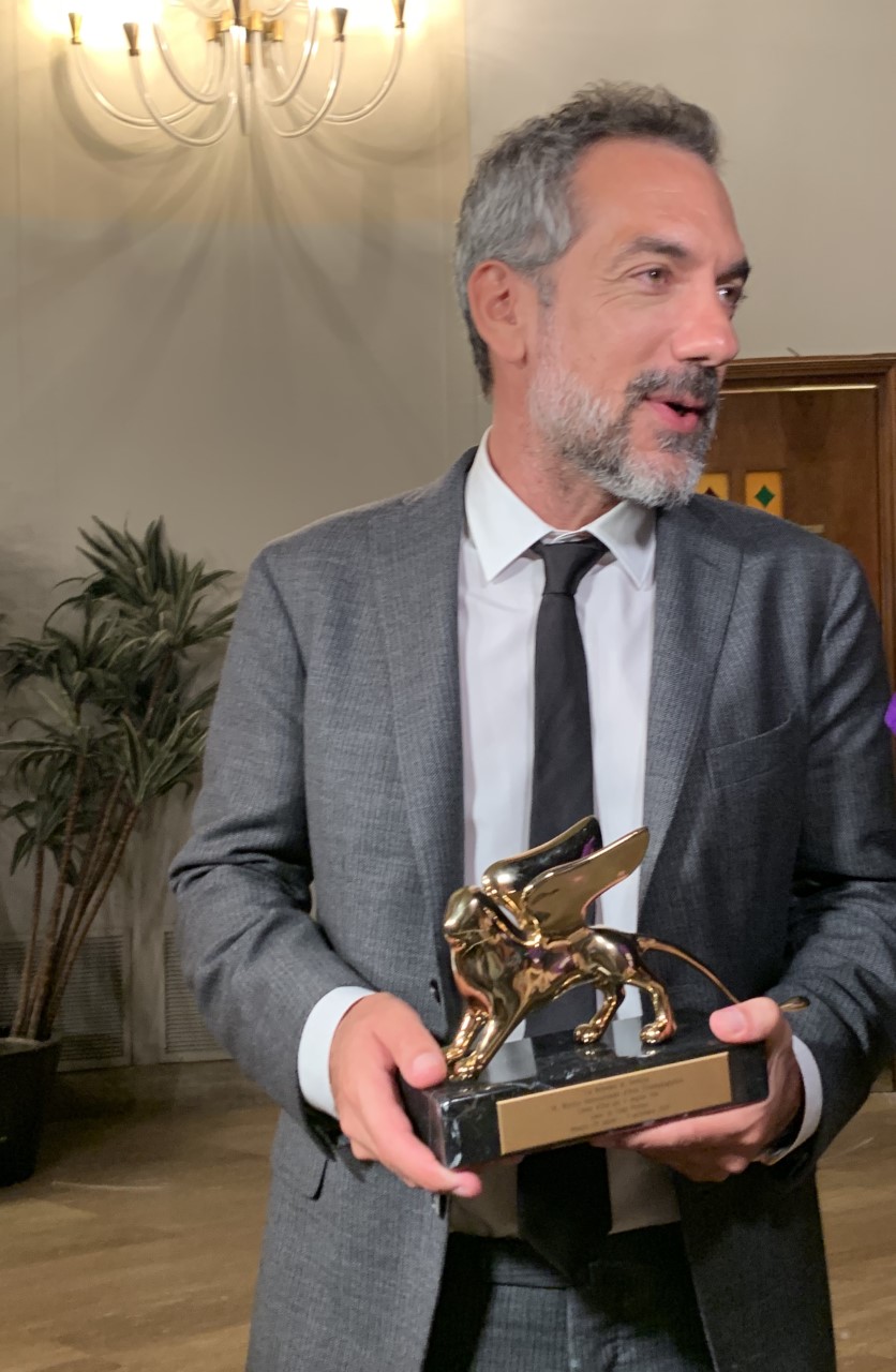 Todd Phillips trzyma Złotego Lwa za Jokera w Wenecji 2019 Todd Phillips w szarym garniturze trzyma statuetkę Złotego Lwa przyznaną filmowi Joker na festiwalu w Wenecji 2019